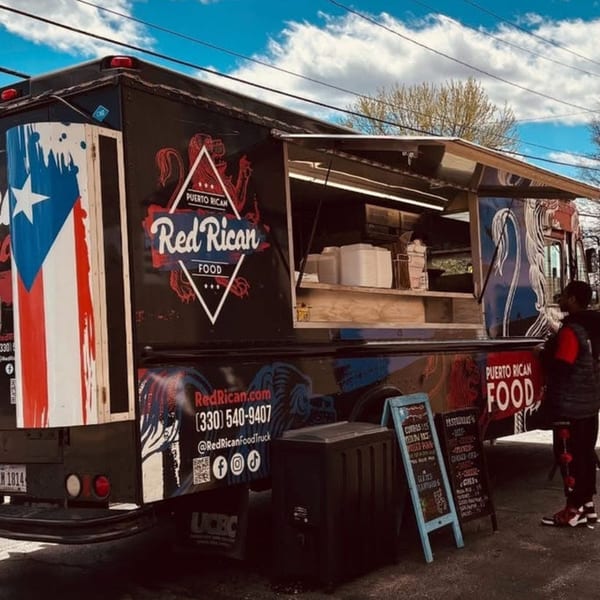The Red Rican food truck, adorned with the Puerto Rican flag, serves customers under a blue sky.