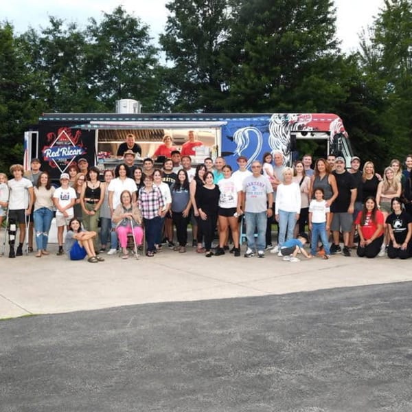 Large group of people posing in front of the Red Rican food truck with trees in the background.