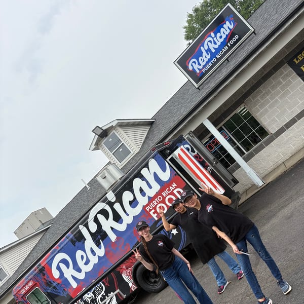 Three Red Rican staff members pose in front of their food truck and restaurant building.
