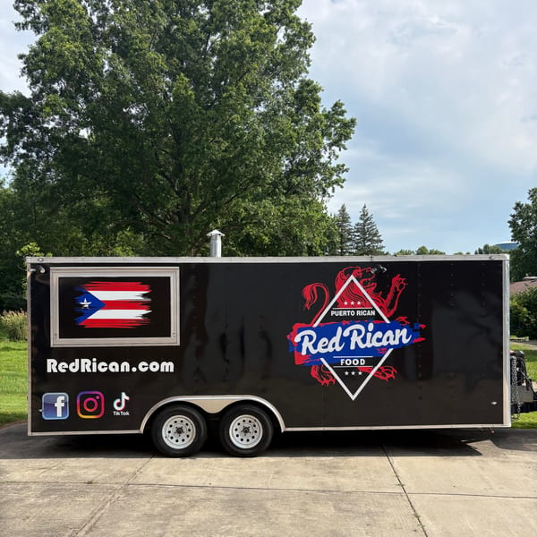 Red Rican food truck, black with a Puerto Rican flag and logo, parked on concrete.