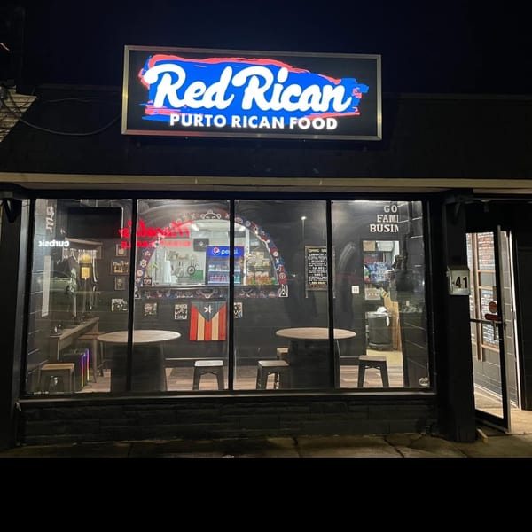 Exterior of Red Rican restaurant at night, with a bright neon sign and visible interior seating.